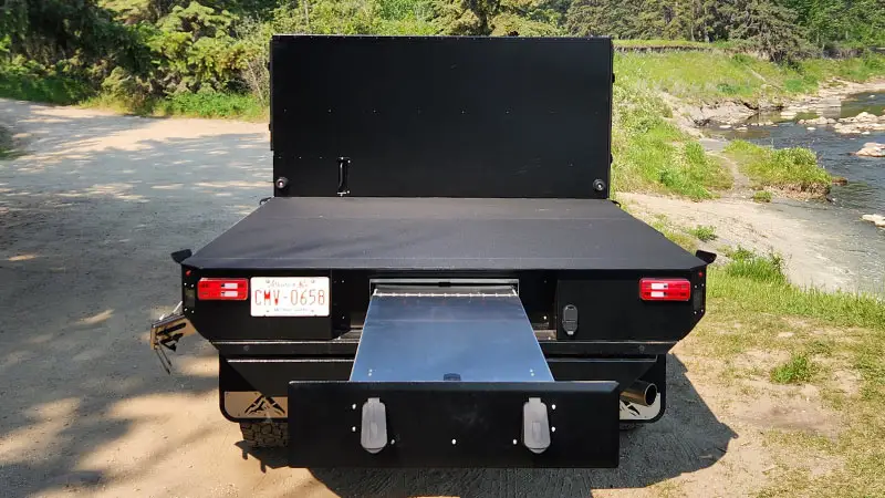 Straight rear view of an Aluma Tray 8 foot aluminum flatbed with the sealed rear drawer pulled out, parked on a gravel bank