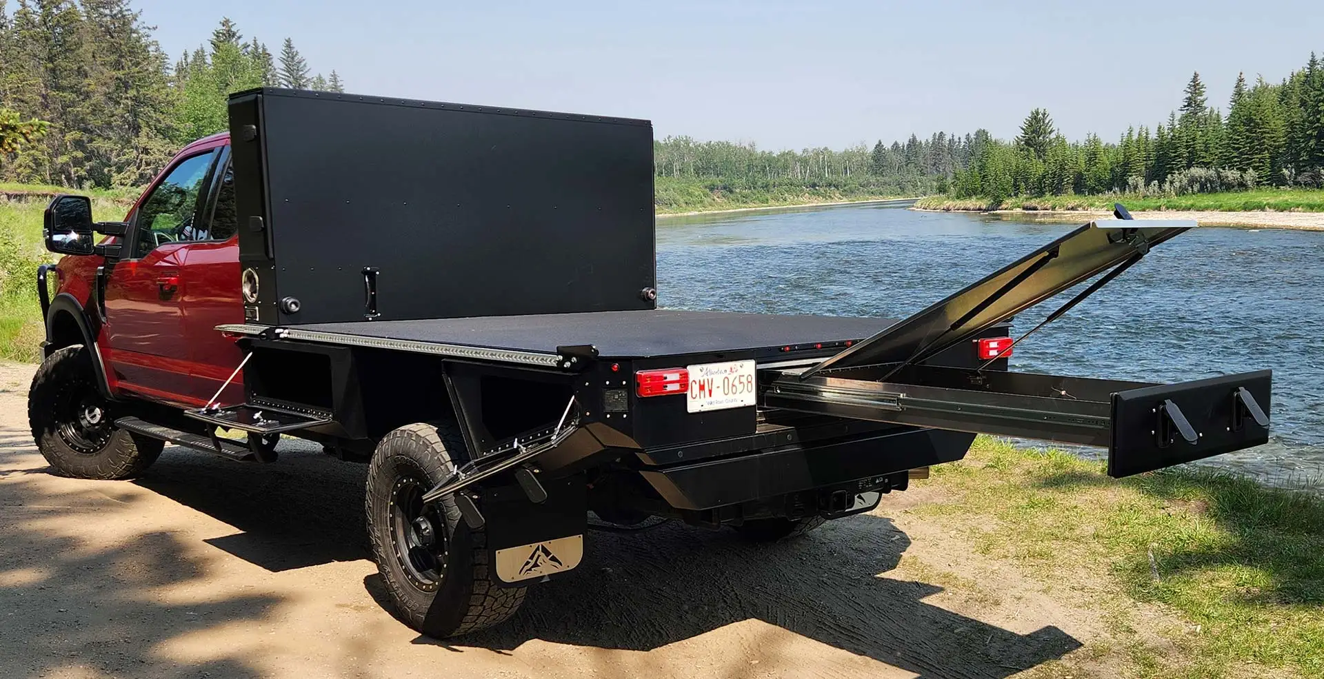 Red Ford Super Duty with an Aluma Tray 8 foot long bed flatbed beside a river, folding stairs extended from the deck