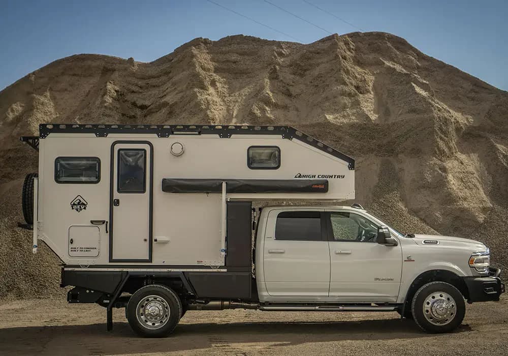 White Ram chassis cab carrying an Aluma Tray HD-60-HC flatbed with a white OEV High Country camper bolted to it, full passenger side profile